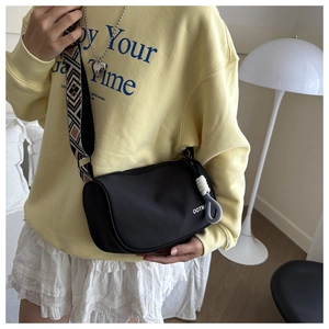 Detail of black nylon barrel crossbody bag with colorful woven strap and rope zip pull