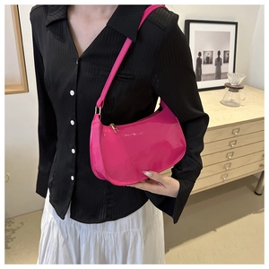 Magenta patent leather baguette bag with gold zipper shown on model in a modern home setting