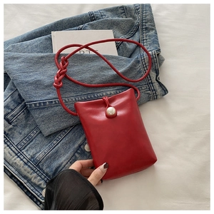 Gros plan d'un mini sac en cuir rouge avec boucle perle sur un jean et un tissu blanc