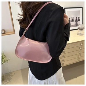 Pink patent leather minimalist underarm bag shown with a model in a modern interior setting