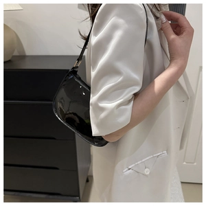 Detail of glossy black patent leather baguette bag with minimalist shoulder strap on model