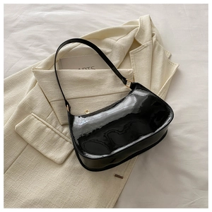 Detail of glossy black minimalist baguette bag with gold metal zipper on a beige blazer