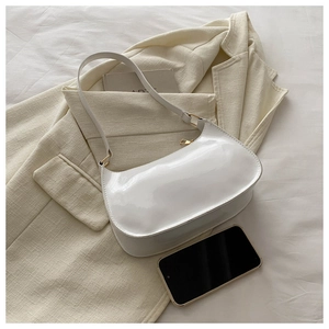 Close-up of white patent leather baguette bag with gold zipper on beige blazer