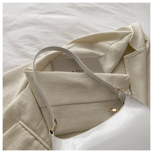 Detail of white glossy leather baguette bag with gold metal zipper on tweed fabric