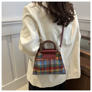 Detail view of plaid crossbody bag with round handle and red leather shoulder strap