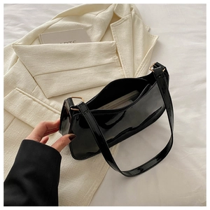 Detail of glossy black patent leather baguette bag with gold metal buckle and zipper