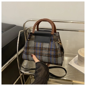 Detail view of plaid wool handbag with resin handles on a glass shelf in cozy setting