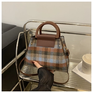 Detail of plaid tweed handbag with leather flap and wood-textured handle on metallic stand