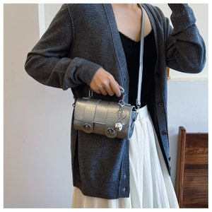 Detail of silver metallic crossbody bag featuring dual twist locks and textured finish