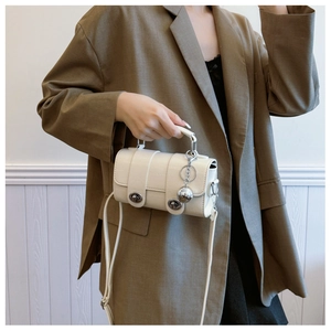 Detail of white crocodile embossed texture handbag with silver ball pendant and metallic lock