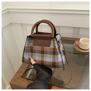 Detail of plaid patterned crossbody bag with elegant round handle and leather flap