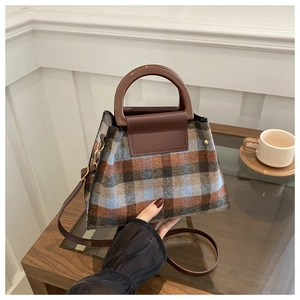 Detail of classic plaid woolen handbag featuring a dark brown round handle and textile texture