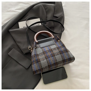 Close-up of retro plaid tweed handbag with wooden handle and leather flap with phone for scale