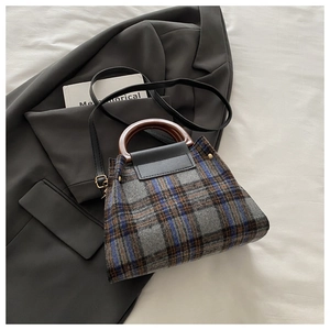 Detail of vintage grey plaid handbag with leather strap on a grey suit background