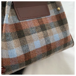 Close-up of wool plaid handbag featuring brown leather patch and gold stud accents