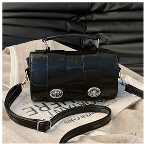 Detail of black faux crocodile texture barrel bag with silver hardware and shoulder strap