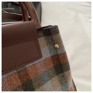 Detail of plaid tweed handbag with brown leather trim and golden metal rivet studs