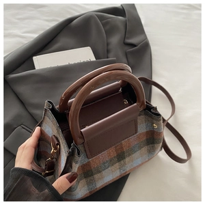 Detailed close-up of British plaid wool fabric texture and sleek dark brown handle on bag