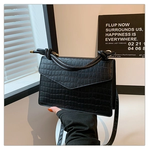 Detail of black crocodile texture bag with unique knotted handle and flap closure