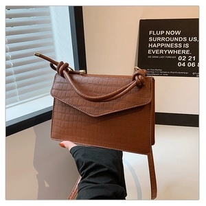 Detail of brown crocodile pattern shoulder bag featuring knotted strap and metal closure