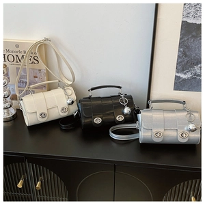 Three elegant leather bags in white, black and silver displayed on a shelf with metal charms
