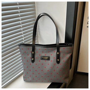 Detail of grey canvas tote with red polka dots and black leather handles in sunlight