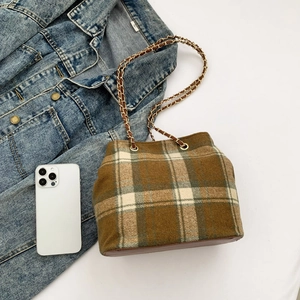 Close-up of brown plaid bucket bag with gold chain strap and denim jacket accent