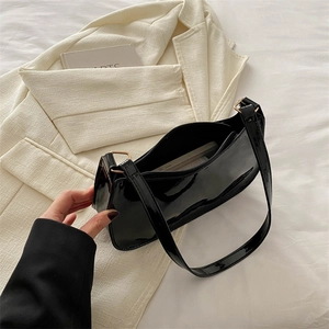 Sleek black patent leather baguette bag with gold hardware on white textured blazer