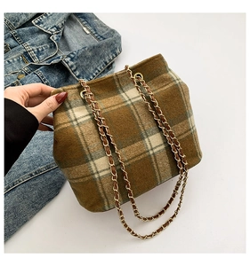 Detailed view of brown plaid woolen bucket bag with gold chain strap on denim jacket