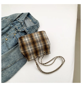Detail of vintage plaid bucket bag with gold chain strap on blue denim background