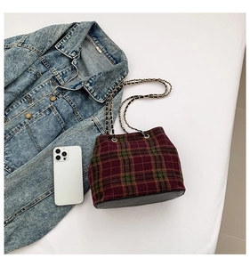Detail of red and green plaid crossbody bag with gold chain strap and black leather base