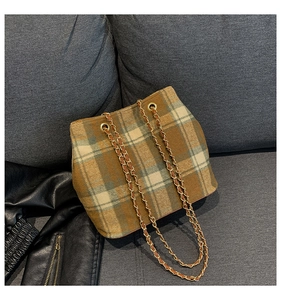 Detail of tartan check crossbody bucket bag with gold chain strap on grey sofa