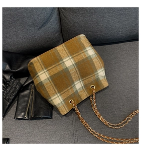 Close-up of retro plaid wool bucket bag with gold chain strap on a grey textured sofa