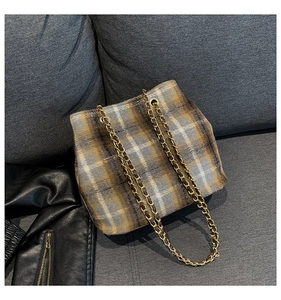 Detail of classic plaid pattern and golden chain strap on a plush textured bucket bag