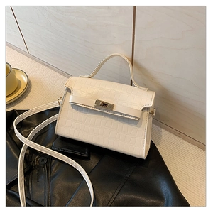 Detail of creamy white crocodile pattern handbag with golden twist lock on black surface