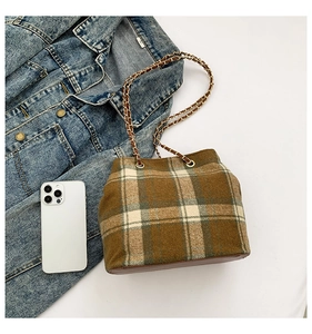 Macro shot of brown plaid bucket bag with woven metal chain strap and leather base detail