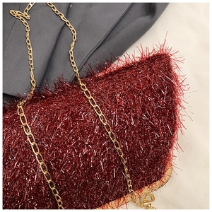 Macro shot of burgundy fringe texture on evening bag with gold chain and metal frame