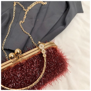Detail of burgundy plush evening bag with gold floral handle and velvet texture