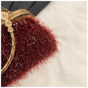 Close-up of red velvet evening bag featuring a gold floral embossed frame and round handle