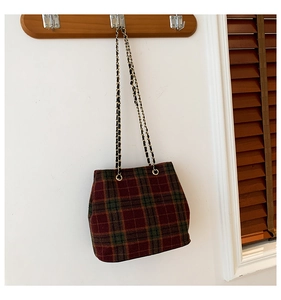 Detail of red and green plaid tote bag with gold chain strap on wooden rack
