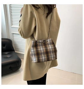 Detail of vintage plaid bucket bag with gold chain strap worn over a camel coat
