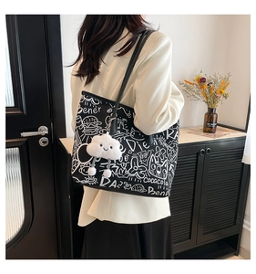 Detail of black tote bag with white graffiti patterns and a plush cloud charm accessory