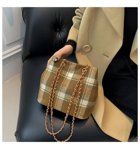 Close-up of classic plaid bucket bag with gold chain strap on camel wool coat
