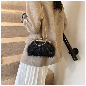 Close-up of black feather clutch bag with gold metal frame and chain on shoulder