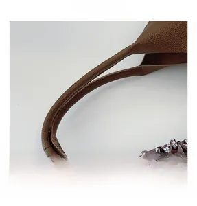 Detail of lychee pattern leather handle with brown plaid woven ribbon on a bucket bag