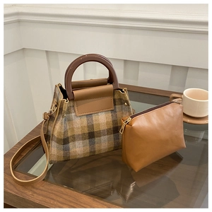 Détail du sac cabas en laine à carreaux et pochette marron sur une table en bois cosy