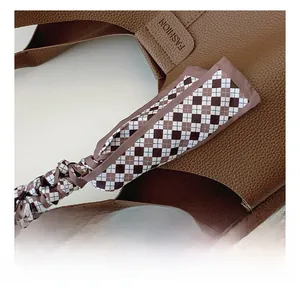 Close-up of brown pebbled leather bucket bag featuring a checkered silk scarf on the handle
