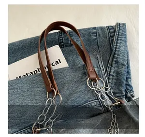 Detail of blue denim tote bag with brown leather handle and silver chain attachment
