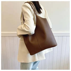 Detail of a large brown pebbled leather tote bag worn as a shoulder bag on a white blazer