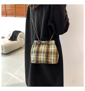 Vue détaillée du sac seau en laine à carreaux avec chaîne dorée sur un manteau noir